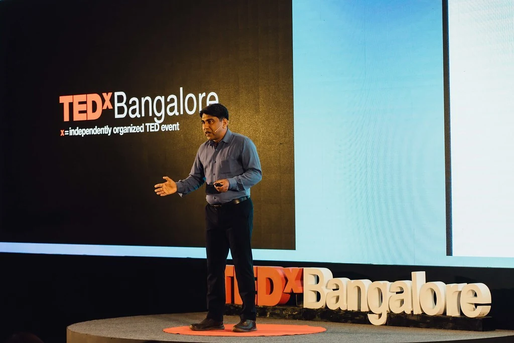 A speaker presenting beside the TEDxBangalore letters at Beyond Resilience.