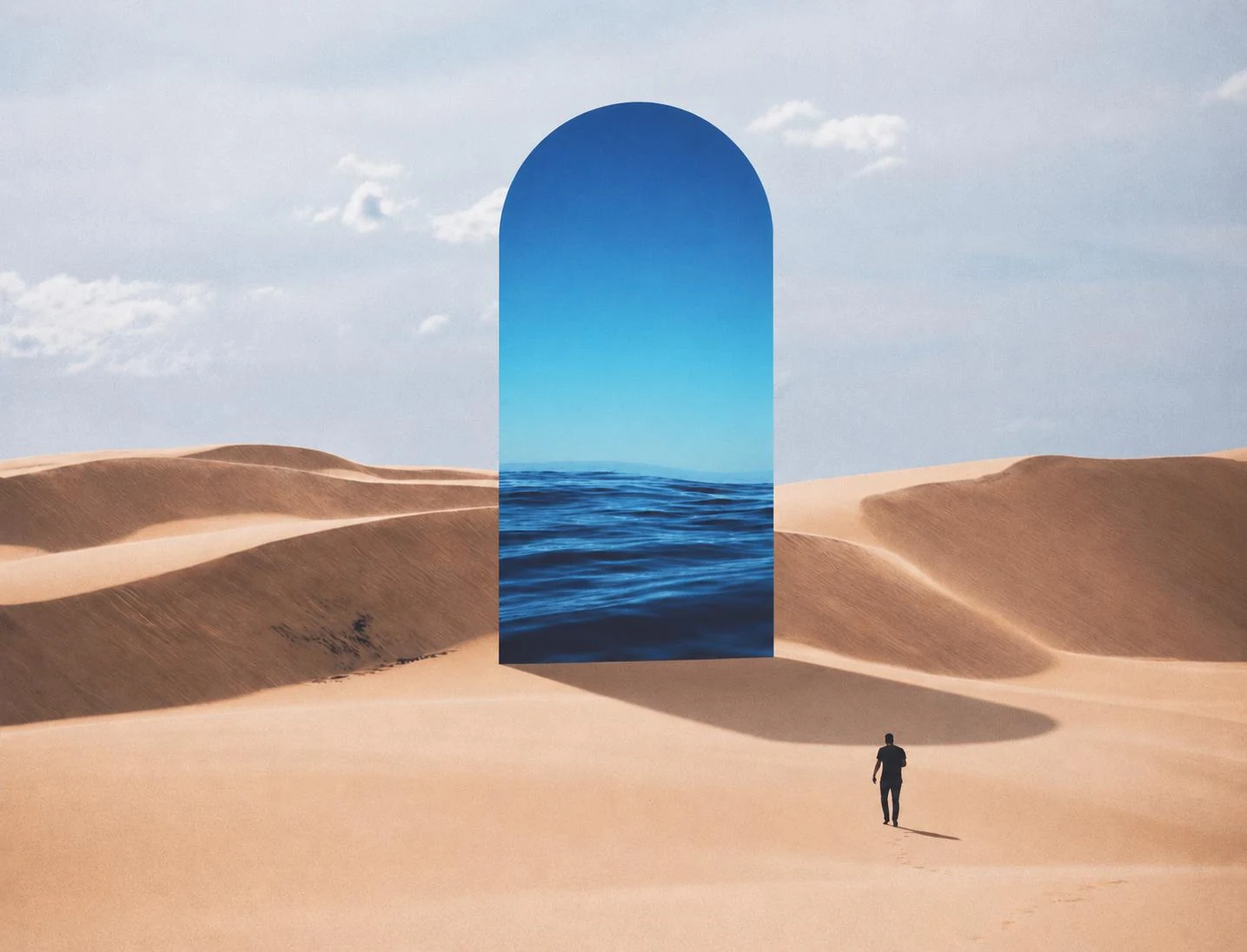 An ocean appears within an immense arched doorway in a sunlit desert